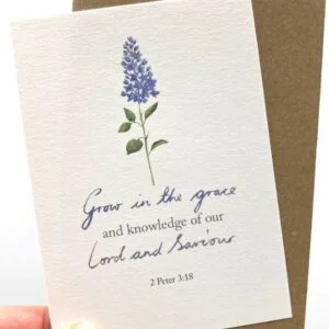 A hand holding the notecard with a flower design and the scripture text